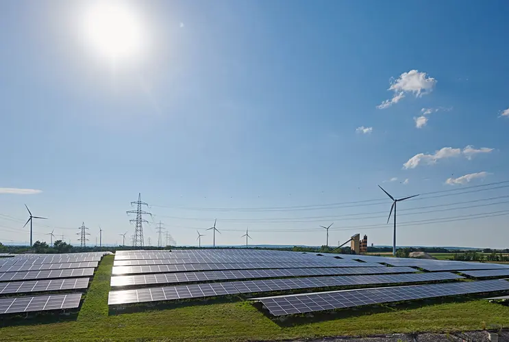 Wir blicken auf einige Windräder, Strommasten und Photovoltaik-Panele bei strahlendem Sonnenschein.