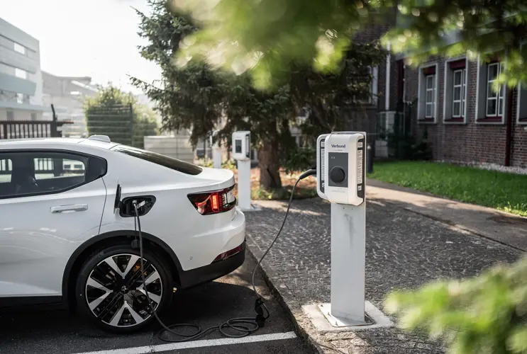 Wir sehen ein weißes E-Auto, das gerade an einer VERBUND-E-Ladestation aufgeladen wird.