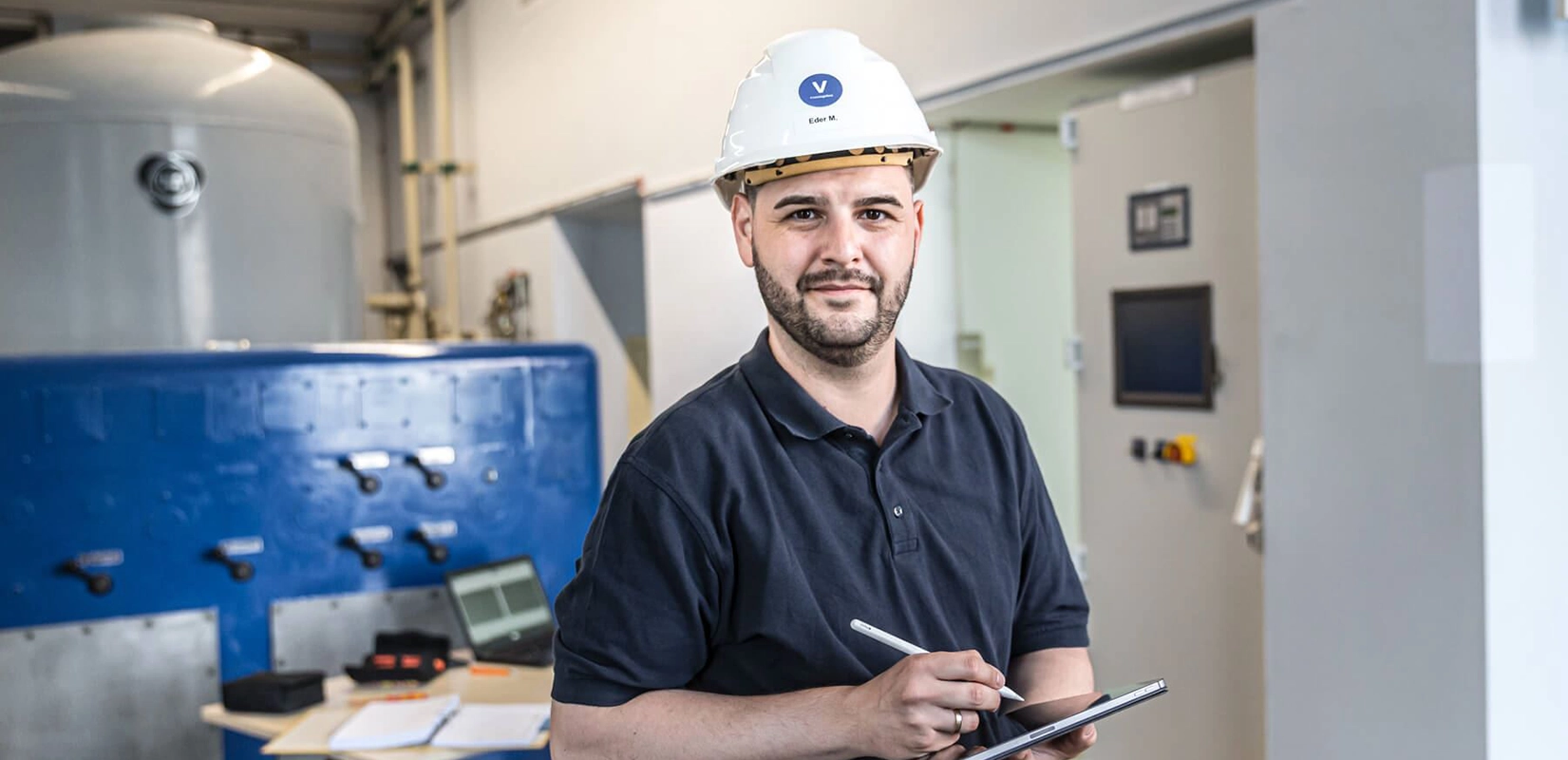 Ein Elektrotechniker des Wasserkraftwerks Rosenheim hält ein Tablet und blickt in die Kamera.