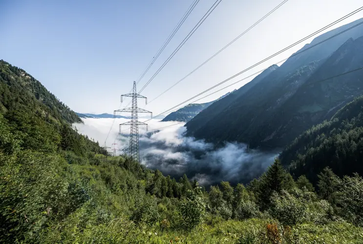 Wir werfen von oben einen Blick in ein nebelverhangenes Tal, das sich saftig grün präsentiert. Im Zentrum sieht man einen Strommasten.