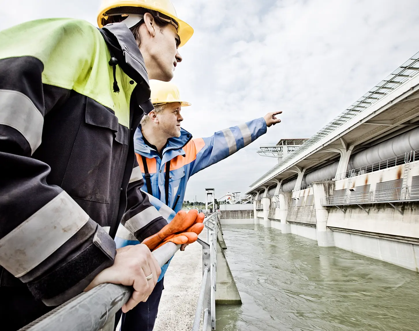 Zwei VERBUND-Wasserkraftwerks-Mitarbeiter blicken auf ein Wasserkraftwerk und beraten sich.