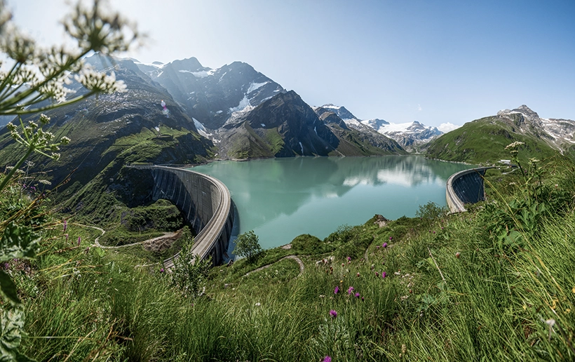 Der Kapruner Stausee mit seinen Gebirgen im Hintergrund bei strahlenden Sonnenschein aus der Vogelperspektive.