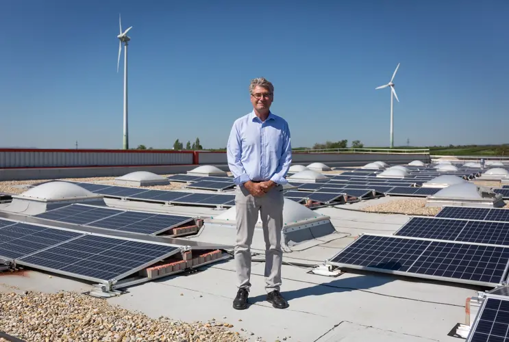 Ein VERBUND-Geschäftspartner steht auf dem Gebäude des Unternehmens und lächelt in die Kamera. Im Hintergrund sieht man Photovoltaikpanele.