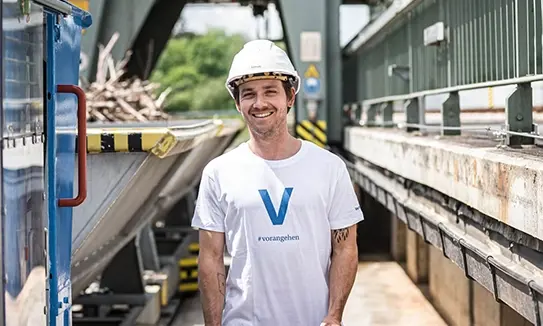 VERBUND-Mitarbeiter Robert Schießl aus dem Kraftwerk Rosenheim trägt auf diesem Foto einen Helm und ein weißes T-Shirt mit einem blauem V drauf.